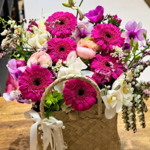 Magenta gerbera, pink ranunculus and orchid arrangement in a woven flower basket in Auckland.