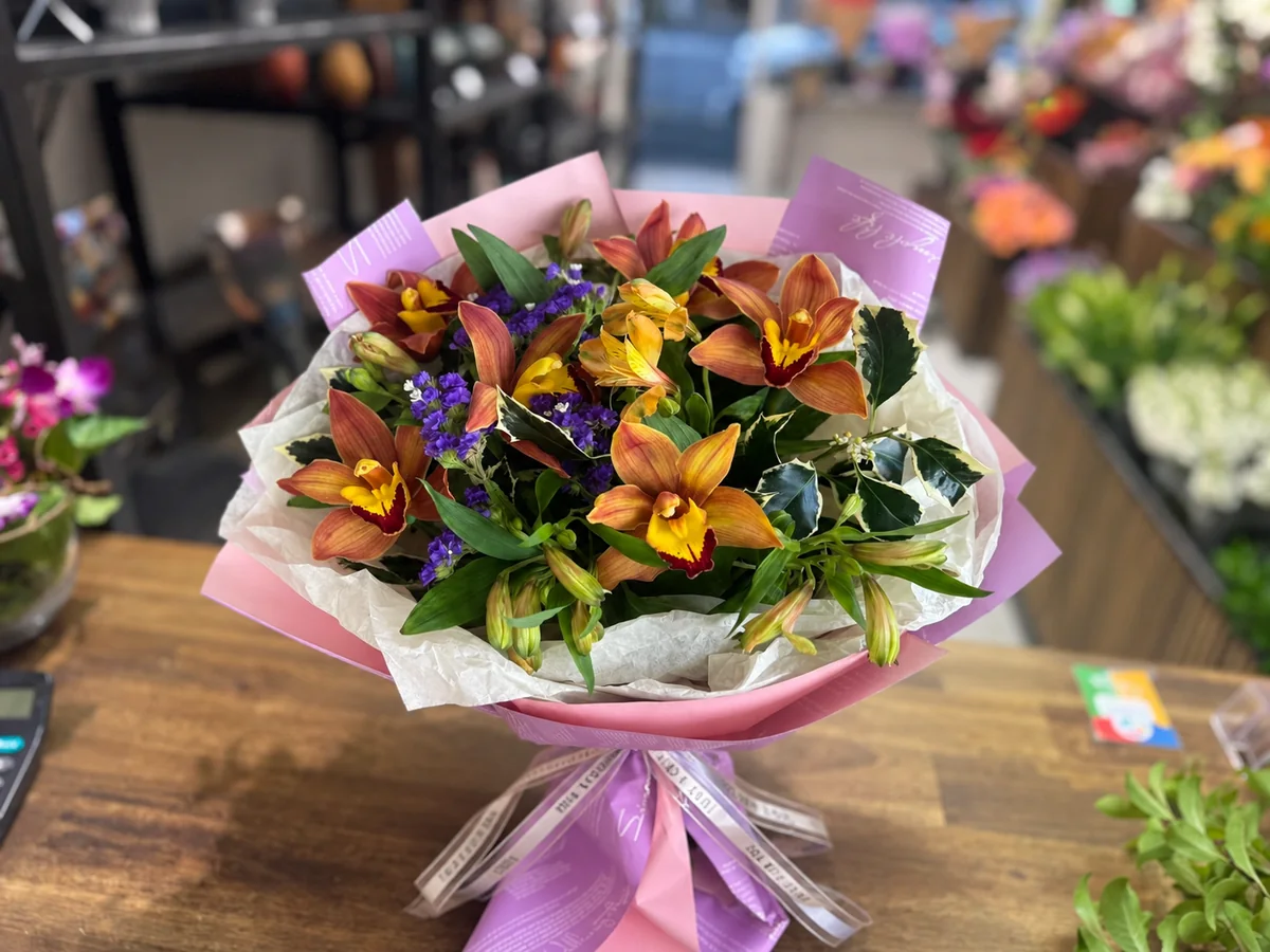Warm autumn bouquet with bronze cymbidium orchids, orange alstroemeria, purple statice and glossy greenery