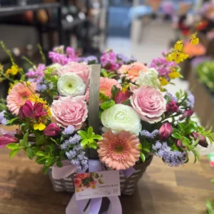 Pastel flower basket with peach gerberas, pink roses, ranunculus, lilac flowers and greenery