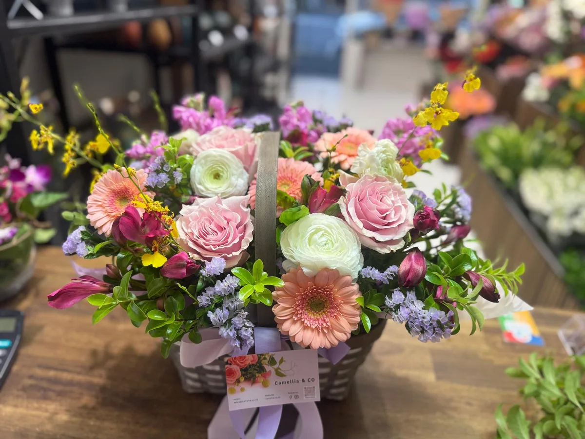 Pastel flower basket with peach gerberas, pink roses, ranunculus, lilac flowers and greenery