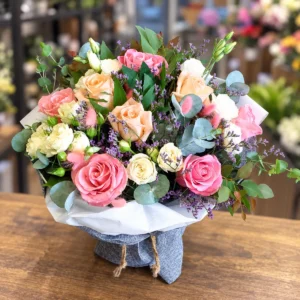 Pastel bouquet with pink and peach roses, cream lisianthus, eucalyptus and delicate purple filler flowers