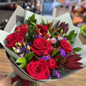 Deep red rose bouquet with burgundy foliage, purple statice and mixed seasonal flowers