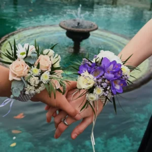Two blush and purple floral wrist corsages held over a fountain