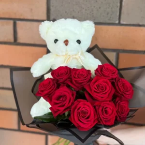 White teddy bear presented with a bouquet of red roses